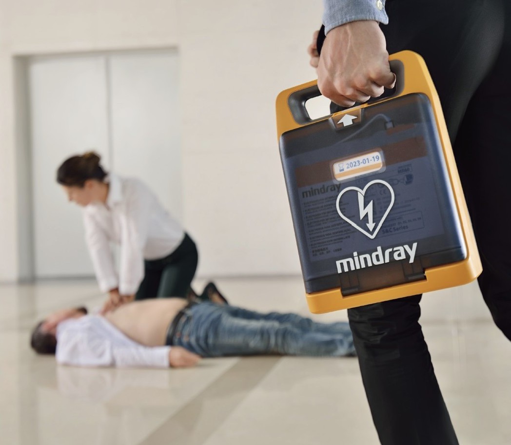 En man som drabbats av hjärtinfarkt ligger orörlig medan en kvinna utför HLR. En tredje person anländer med hjärtstartare